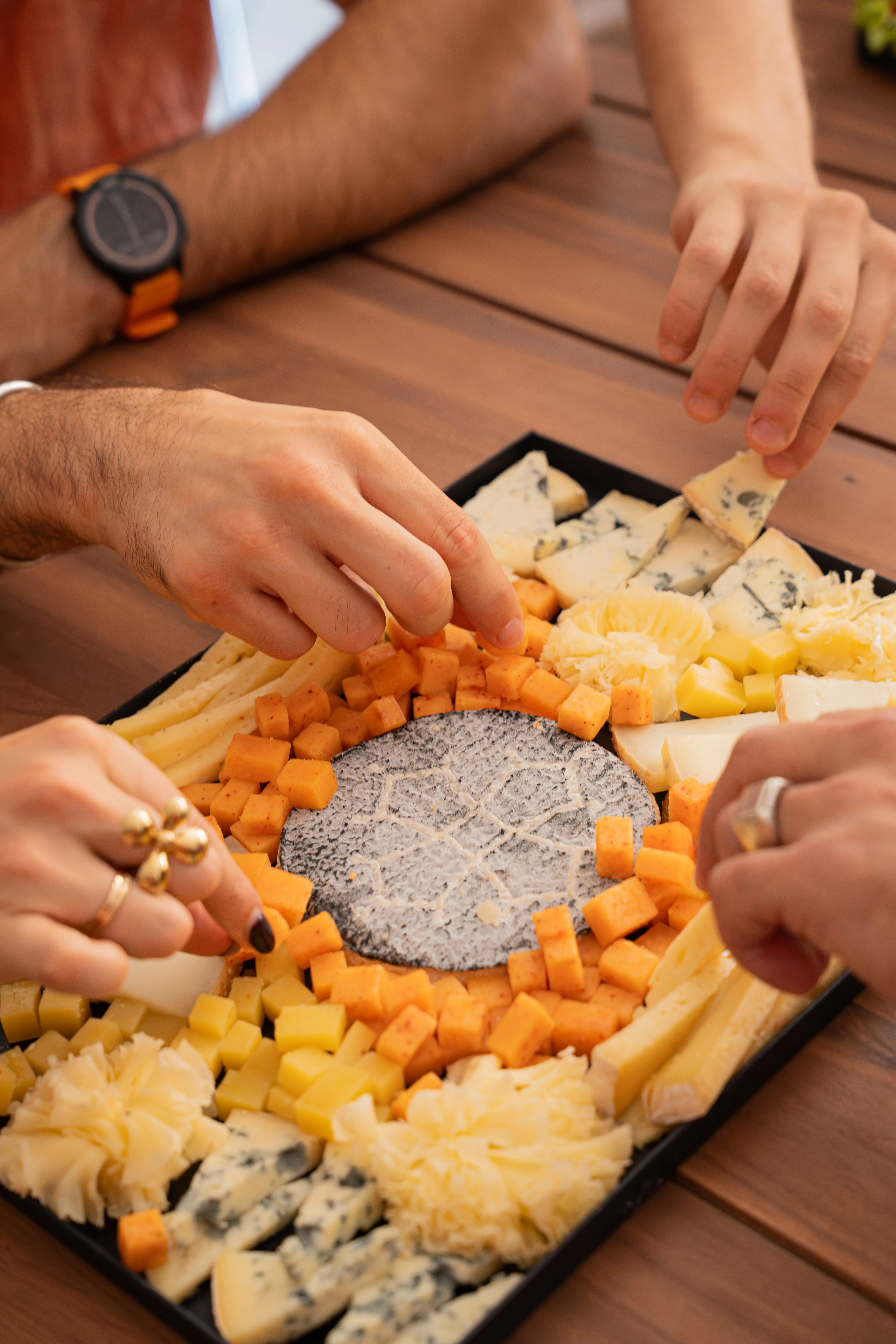 Plusieurs convives se servant sur une planche de fromages